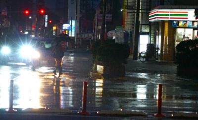 雨によって視界が悪くなり、前方の車や歩行者や白線が見えにくくなっている風景