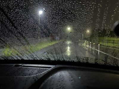 夜間の大雨で窓ガラスに水滴が無数に付着し、街灯の光が乱反射して路面や白線が非常に見えにくくなっている運転席からの風景