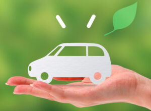 手のひらに乗った白い車の切り絵と葉のイラスト。安心・安全な運転サポートのイメージ