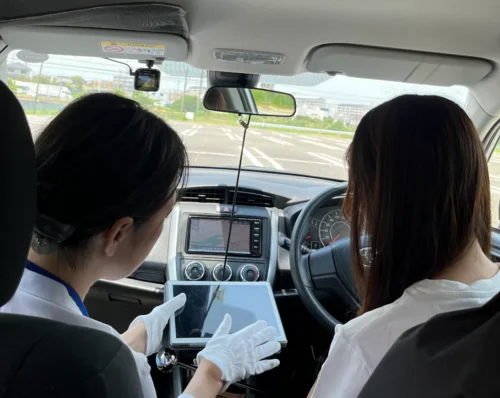 愛知県の出張教習ハーモニーにて、女性インストラクターがタブレットを使用して分かりやすく運転のコツを指導している様子。