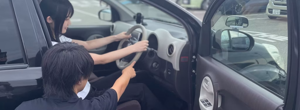 運転席の受講生に対し、インストラクターが車外からハンドルや計器の操作方法を丁寧に説明しているペーパードライバー教習の様子
