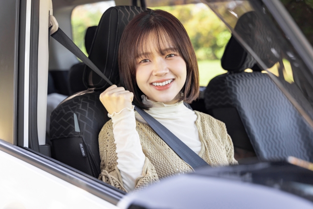 シートベルトを正しく着用し、運転席で笑顔でガッツポーズをする女性。ペーパードライバー講習の安心感をイメージ。